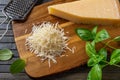 Grated parmesan cheese on a cutting board. Italian grana padano cheese whole and grated, grater and fresh basil herb over wooden