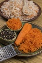 Grated raw carrots, grater and peppercorn in plate. Salted cabbage