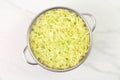 Grated salted zucchini placed in a steel microperforated colander, for straining out the water of them, over marble white kitchen