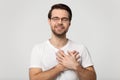Grateful man in glasses feel thankful keeping hands on chest