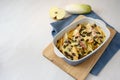 Gratin from endives or chicory with apple, ham, cheese and pumpkin seeds in a baking casserole on kitchen board and a blue napkin