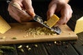 Grating hard cheese with a grater in the hands of a cook for preparing breakfast on the kitchen table. Low key concept for Royalty Free Stock Photo