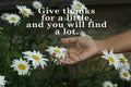 Gratitude inspirational quote - Give thanks for a little, and you will find a lot. With hand holding white daisy flower in garden.