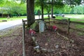 A grave with a white stone headstone surrounded by a brown wooden fence and lush green trees and grass and a log cabin Royalty Free Stock Photo