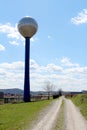 Gravel and dirt country road with grass in middle surrounded with wire fence and industrial building next to tall metal shiny Royalty Free Stock Photo