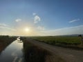 Gravel path on a green rice field plain landscape with yellow sun rising on a blue sky in Pals, Catalonia Royalty Free Stock Photo