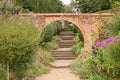 A gravel path passes through a circular archway in an old brick wall, which leads on to some old brick steps in an English country