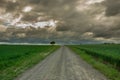 Gravel road through green fields and dark clouds in the sky Royalty Free Stock Photo