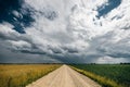 Gravel road in the middle of green and yellow fields and stormy clouds above it Royalty Free Stock Photo