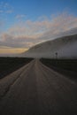 Gravel road through tundra landscape along a mountain during mystical misty morning