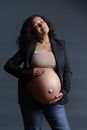 Gravid woman, expectant mother strokes her pregnant belly over gray background. 40 week of happy carefree pregnancy.