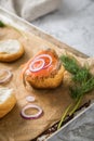 Gravlax a raw, marinated graved salmon with dill on bred roll bun with cream cheese, onion rings on tray with baking paper and