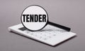 On gray background black calculator and magnifier with text TENDER. Business concept