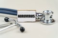 On a gray background, a stethoscope and a cardboard sign with the inscription - Norovirus