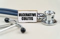 On a gray background, a stethoscope and a cardboard sign with the inscription - Ulcerative colitis