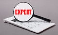 On a gray background, a white calculator and a magnifying glass with the text EXPERT. Business concept