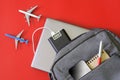 Gray backpack with gadgets: laptop, mobile phone, power bank, notepad and pen on red background next to toy airplanes. Concept of Royalty Free Stock Photo