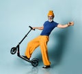 Aging man in t-shirt, sunglasses, orange pants, hat, gumshoes. Riding black scooter, smiling, posing on blue background Royalty Free Stock Photo