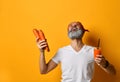 Mature male in red bandana, white t-shirt and bracelet. He laughing, holding glass of juice, carrots, posing on yellow background Royalty Free Stock Photo