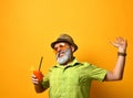 Gray-bearded man in hat, green shirt, sunglasses. Smiling, stretching himself, holding glass of juice, posing on orange background Royalty Free Stock Photo