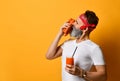 Mature man in red bandana, white t-shirt and bracelet. He holding glass of juice, sniffing carrots, posing on yellow background Royalty Free Stock Photo