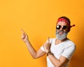 Mature man in sunglasses, red bandana, white t-shirt, bracelet. Pointing at something by forefingers, posing on orange background Royalty Free Stock Photo