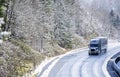 Gray big rig semi truck with covered semi trailer transporting cargo on winter snowing road with wet surface Royalty Free Stock Photo