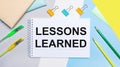 On a gray and blue background are stationery of yellow-green color, a notebook with the text LESSONS LEARNED. Flat lay Royalty Free Stock Photo