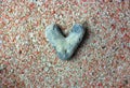 Gray heart-shaped sea stone, rock against the summer pink sand flatly. Love. Royalty Free Stock Photo