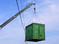 Gray boom with blue hook of truck manipulator lift green cargo container up