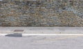 Gray and brown Natural stone bricks wall, a sidewalk and a weathered asphalt road in front. Royalty Free Stock Photo