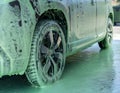 Gray car covered with green foam at a car wash at a self-service station, details of automobile