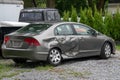 Gray car in a junk yard with damage to the rear panel, door and tire of a gray car due to an automobile accident.