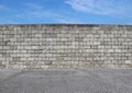 Gray cement block wall with an asphalt street in front and blue sky above.