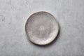 Gray ceramic plate on grey concrete rough background. Empty spotted uneven saucer. Matte dish on stone textured backdrop. Hand