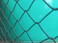 a gray chain-link fence forming a repeating diamond pattern, set against a smooth turquoise-green wall. Royalty Free Stock Photo