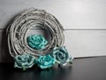 A gray coiled wooden wreath with teal paper roses