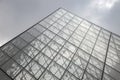 Gray cone of pyramid made of glass and metal against a cloudy sky