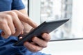 Gray e-reader electronic book in male hands. A man in a blue t-shirt with a tablet against a blurred background