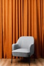Gray easy chair stands against the background of an orange curtain