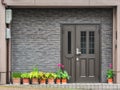 Gray front door with small square decorative windows and flower pots in fron of it