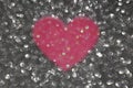 Abstract defocused grey glitter background with a pink heart in the center