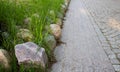 A gray granite-tile pavement with large stones in the green grass along the edge. Royalty Free Stock Photo