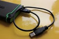 Gray and green external hard drive for backup with USB cable on yellow background with copy space.