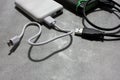 Gray and green external hard drive and white Powerbank battery charger with USB cable on gray concrete background with copy space.