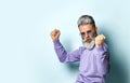 Gray-haired aged man in purple sweater, sunglasses. Dancing with clenched fist while posing on blue studio background. Close up Royalty Free Stock Photo
