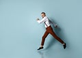 Gray-haired, bearded male in white shirt, brown pants and suspenders, black loafers. He is running against blue background Royalty Free Stock Photo