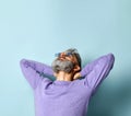 Gray-haired man in purple sweater, sunglasses. Put his hands behind head and looking up, posing on blue background. Close up Royalty Free Stock Photo