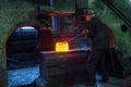 blacksmith worker taking large piece of hot steel with big forceps in old factory