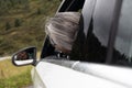 A gray-haired lady sits behind the wheel of a passenger car with an open window and smiles in the side mirror Royalty Free Stock Photo